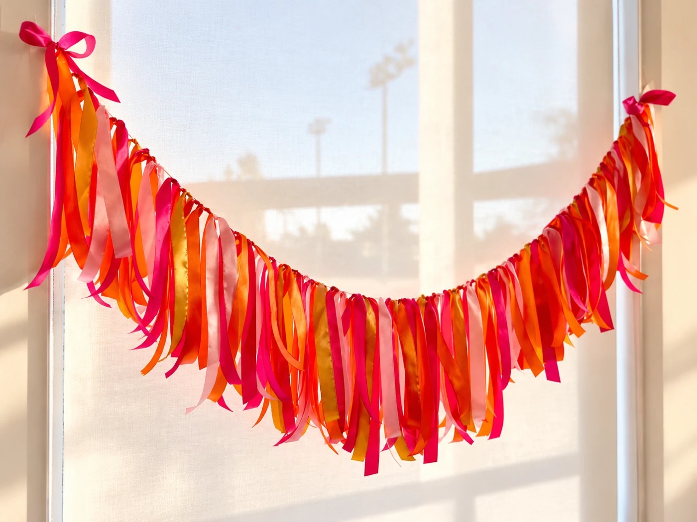 Handmade satin ribbon garland in pink, orange and yellow, hung across a sunlit window
