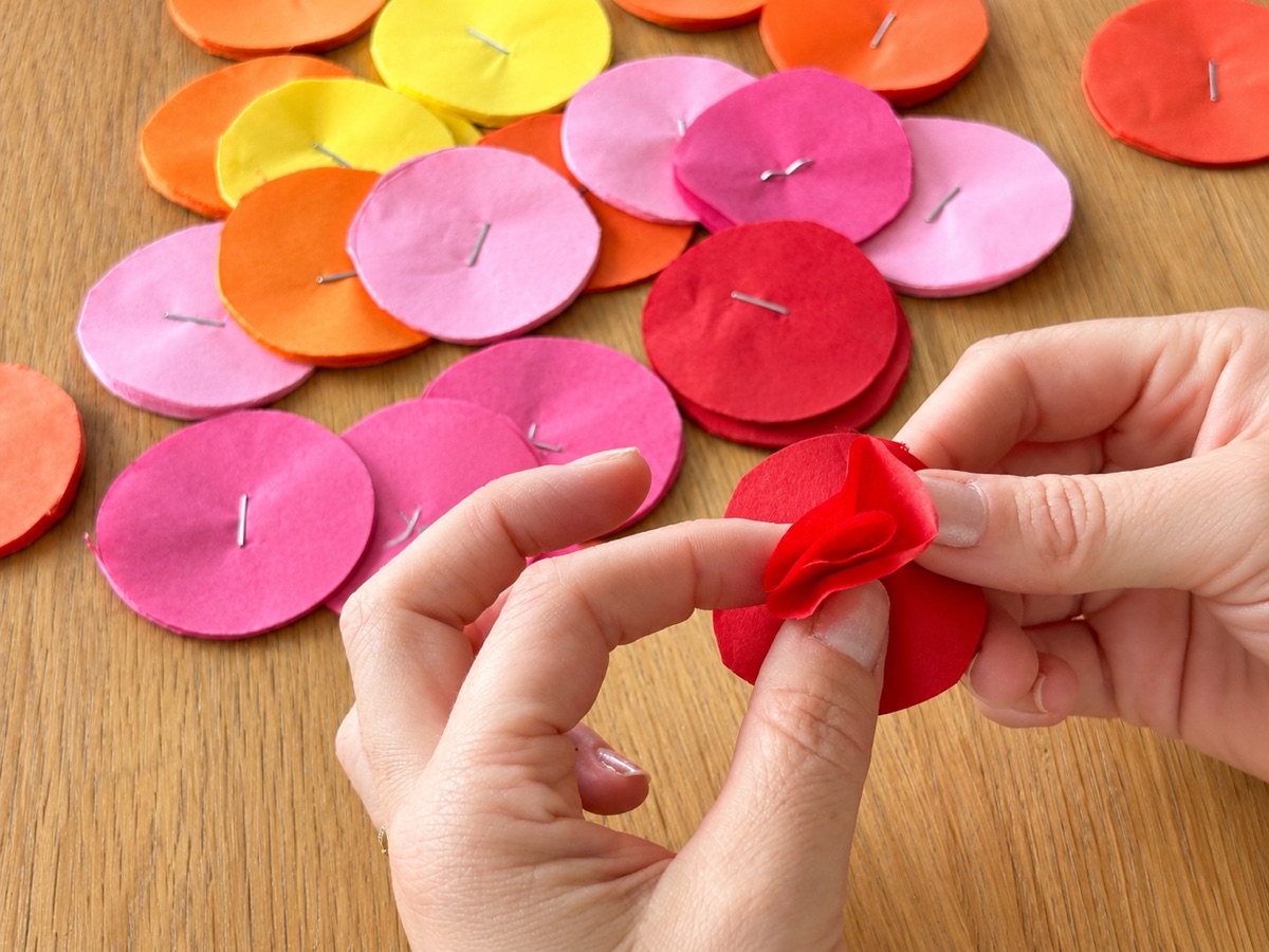 Hands starting to separate the layers of a red tissue paper circle.