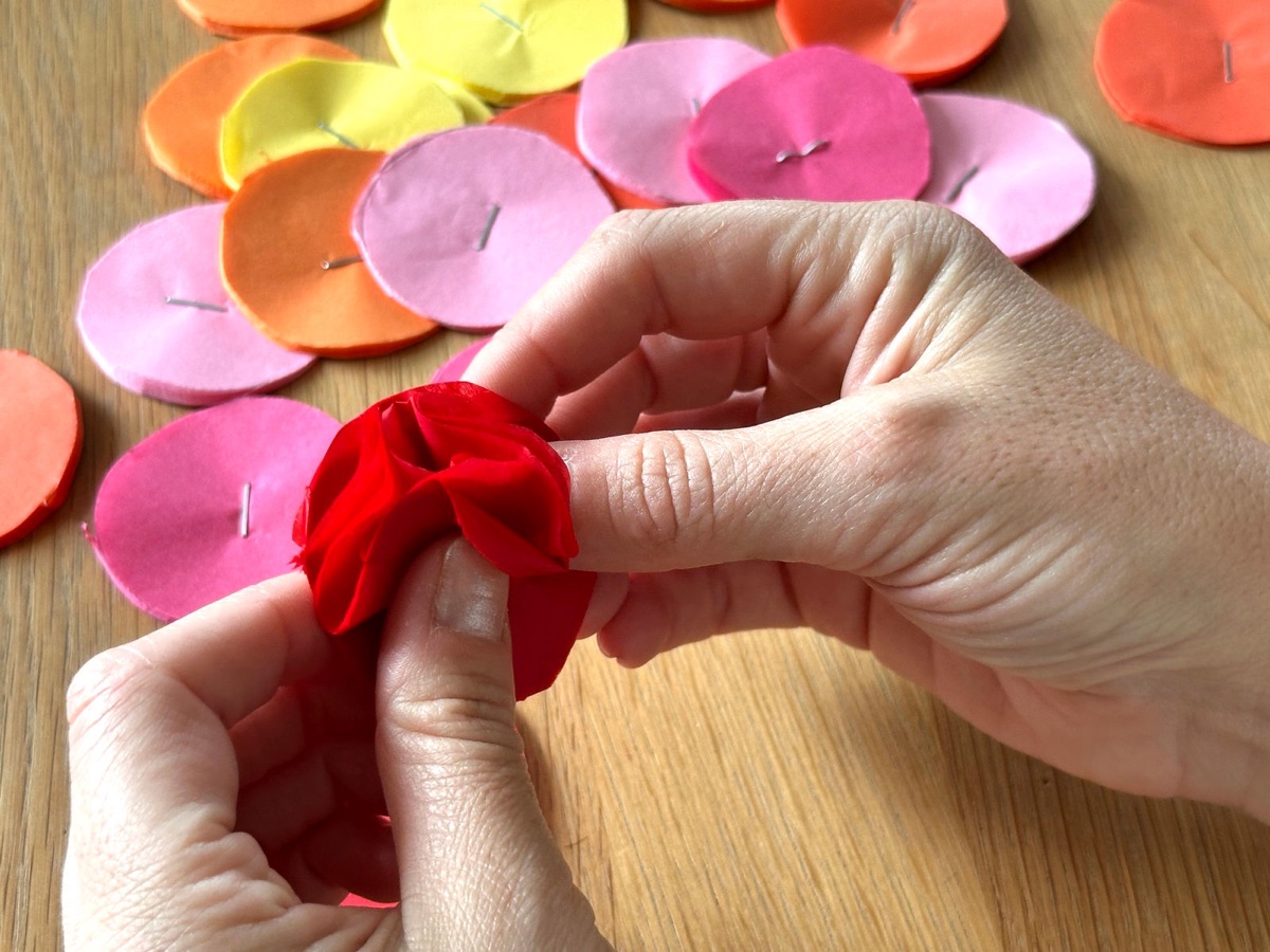 Fluffing a red tissue paper circle layer by layer into a flower.