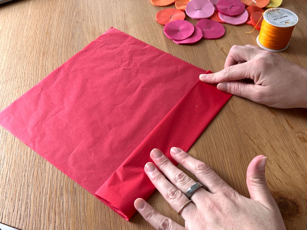 Hands folding a sheet of red tissue paper.