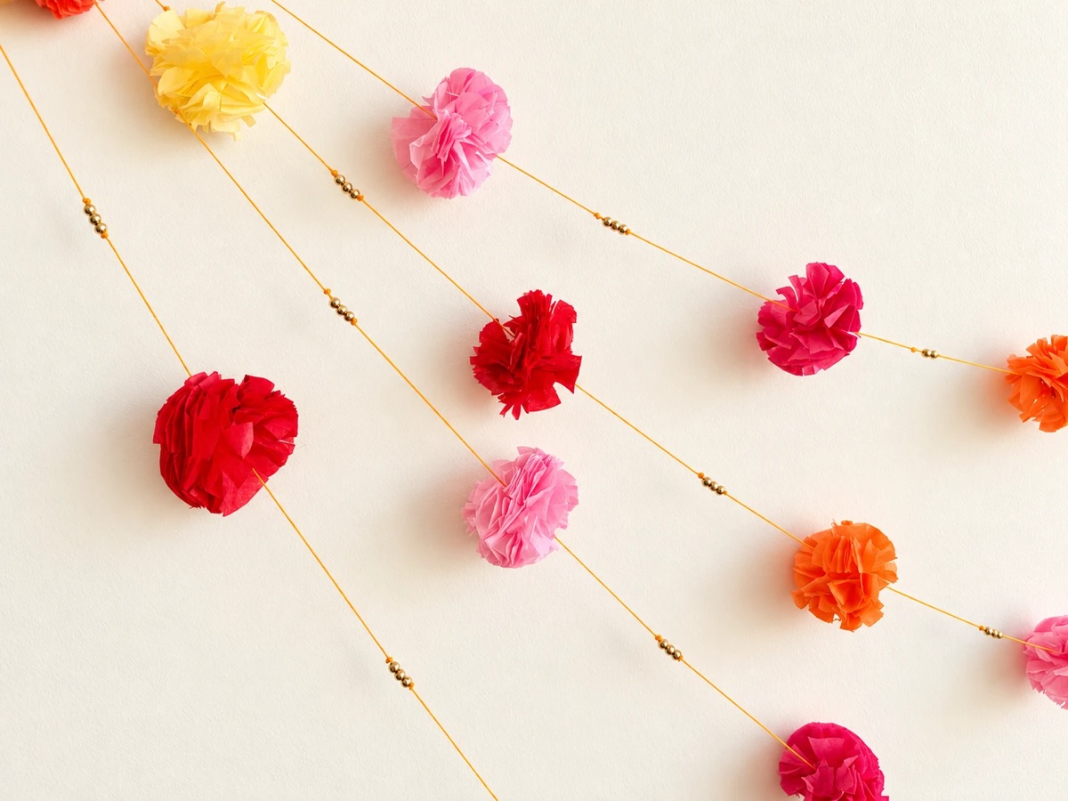 Close-up of hand-fluffed tissue paper marigolds in yellow, pink, red and orange with gold beads on orange cord