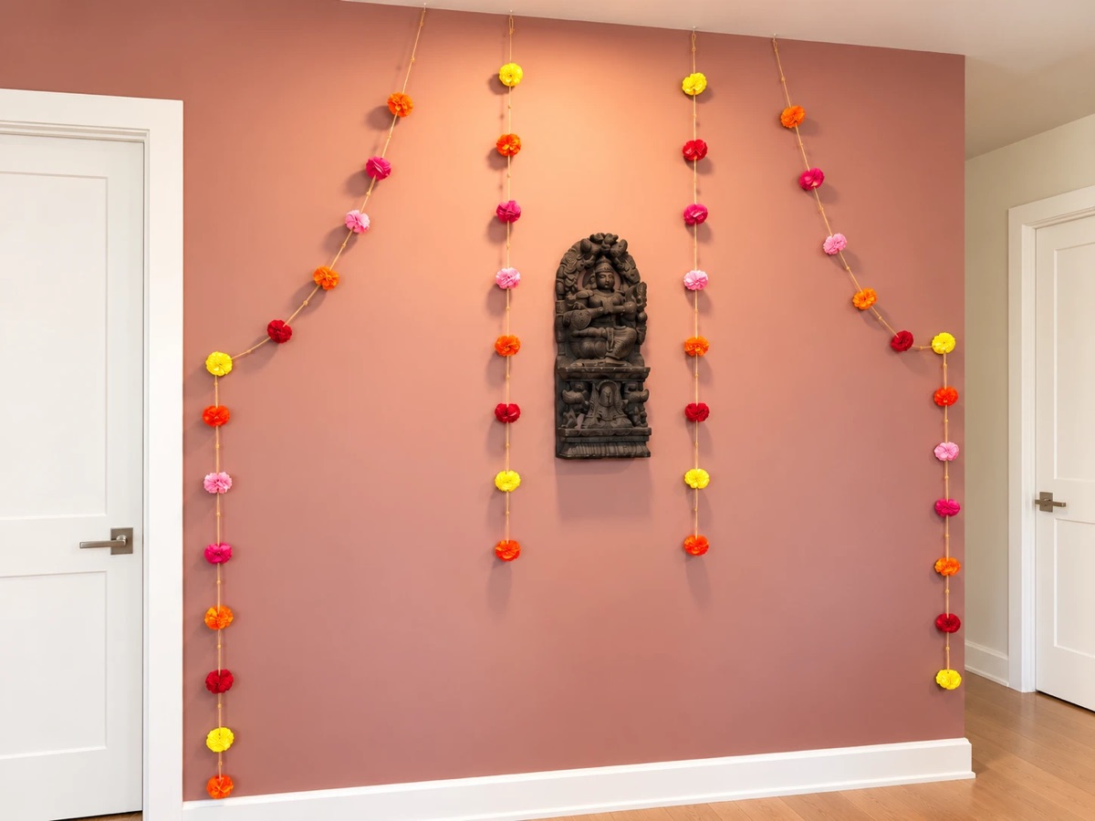 Marigold garlands hung in long strands on a terracotta wall around a carved wooden shrine panel