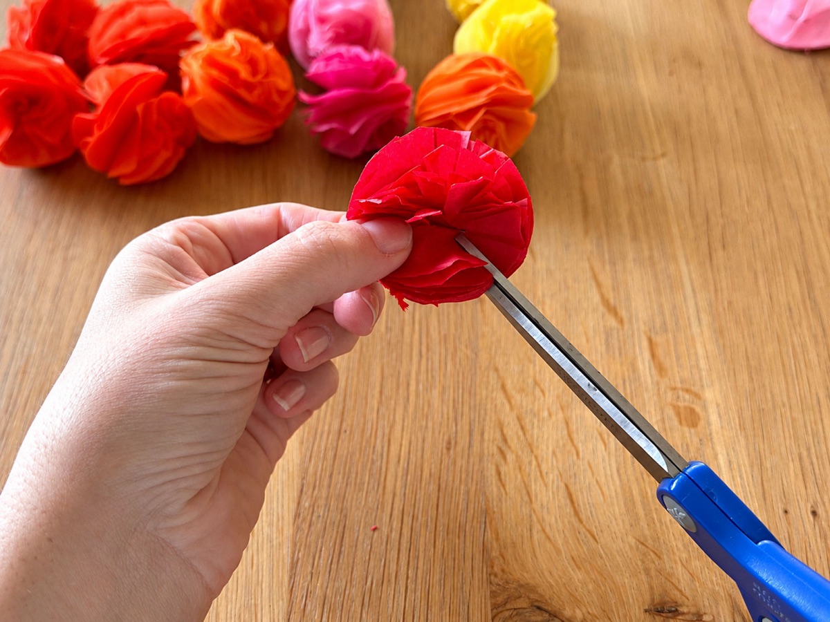 Scissors cutting petal-like fringe into the edge of a red tissue paper flower.