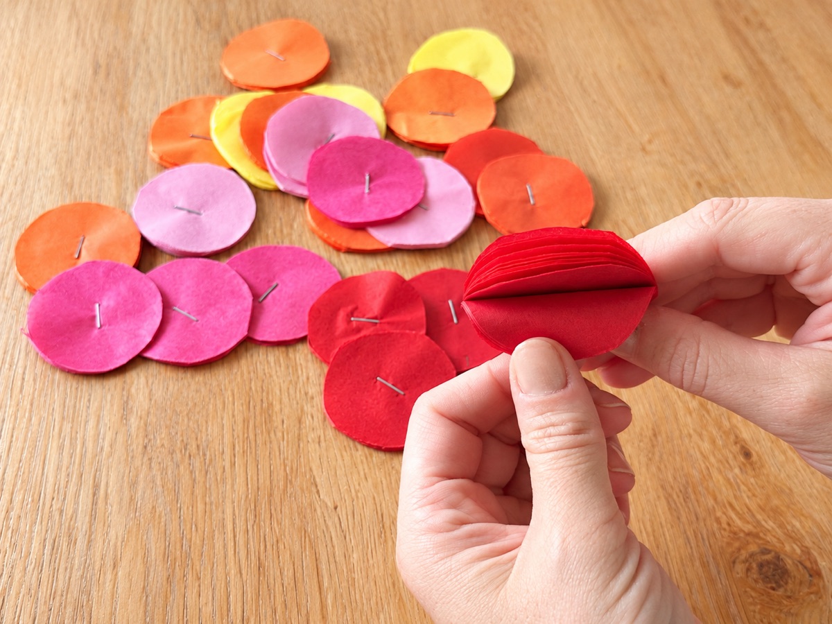 A pile of stapled tissue paper circles in six colors, with a hand holding a red stack to show the layers.