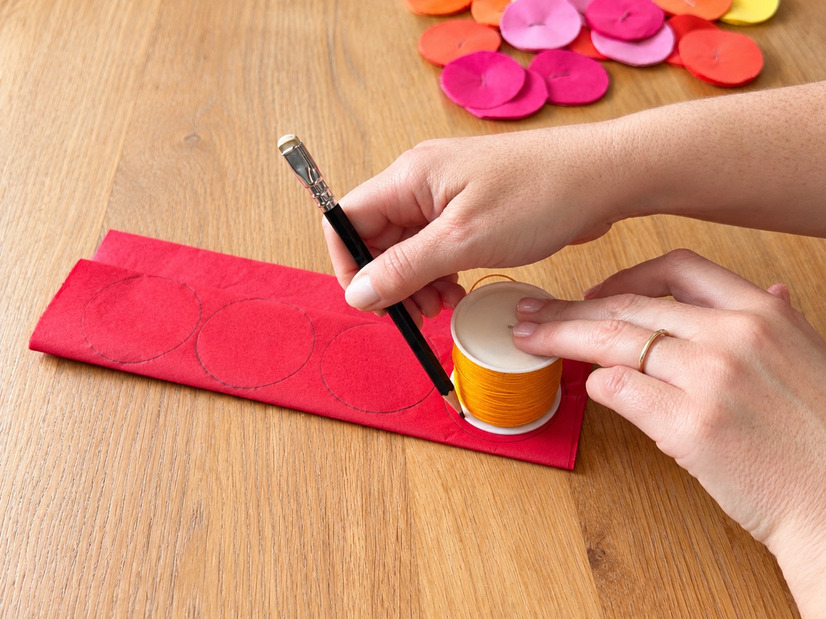 Tracing circles on folded red tissue paper using a spool of cord as the template.